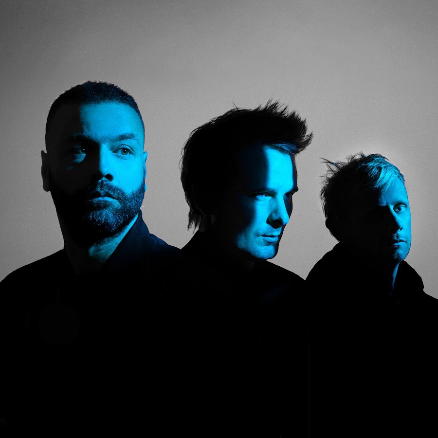 A photo of three men from the band, Muse illuminated with blue light on their face.